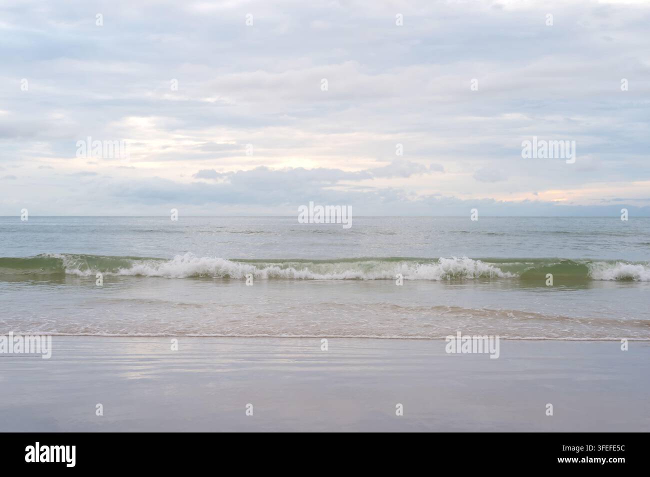 Onde gentili che si infrangono su una spiaggia sabbiosa sotto un cielo nuvoloso. Foto Stock