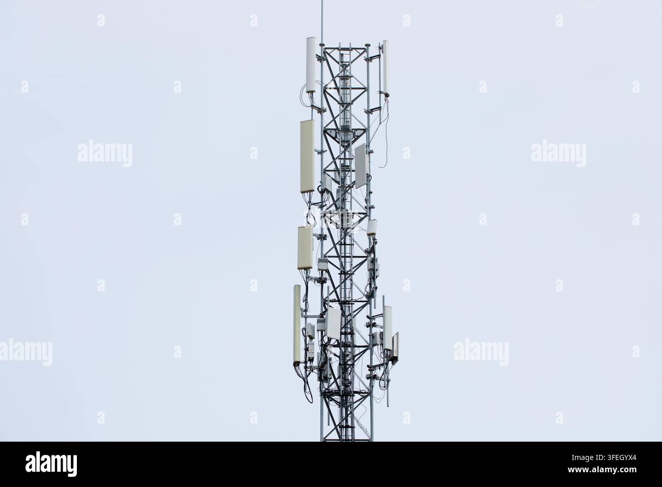 Torre di telecomunicazioni in acciaio si erge contro un cielo blu terso, pannelli antenna allineano la struttura verticale accanto alle attrezzature di segnalazione, simboleggiando il moderno 5G Foto Stock