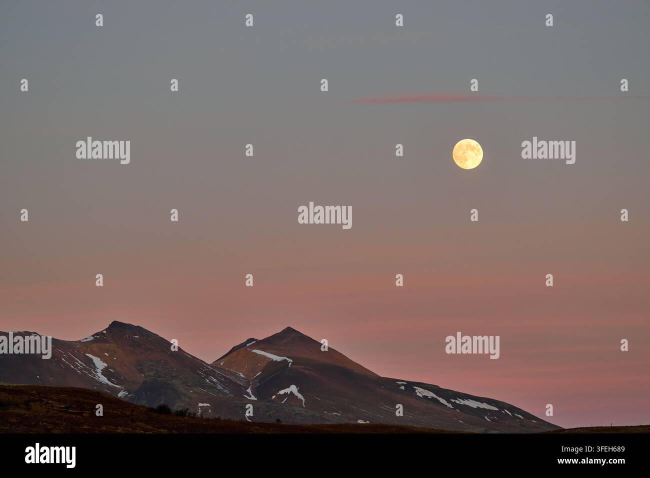 Luna piena che sorge sulle montagne innevate al crepuscolo Foto Stock