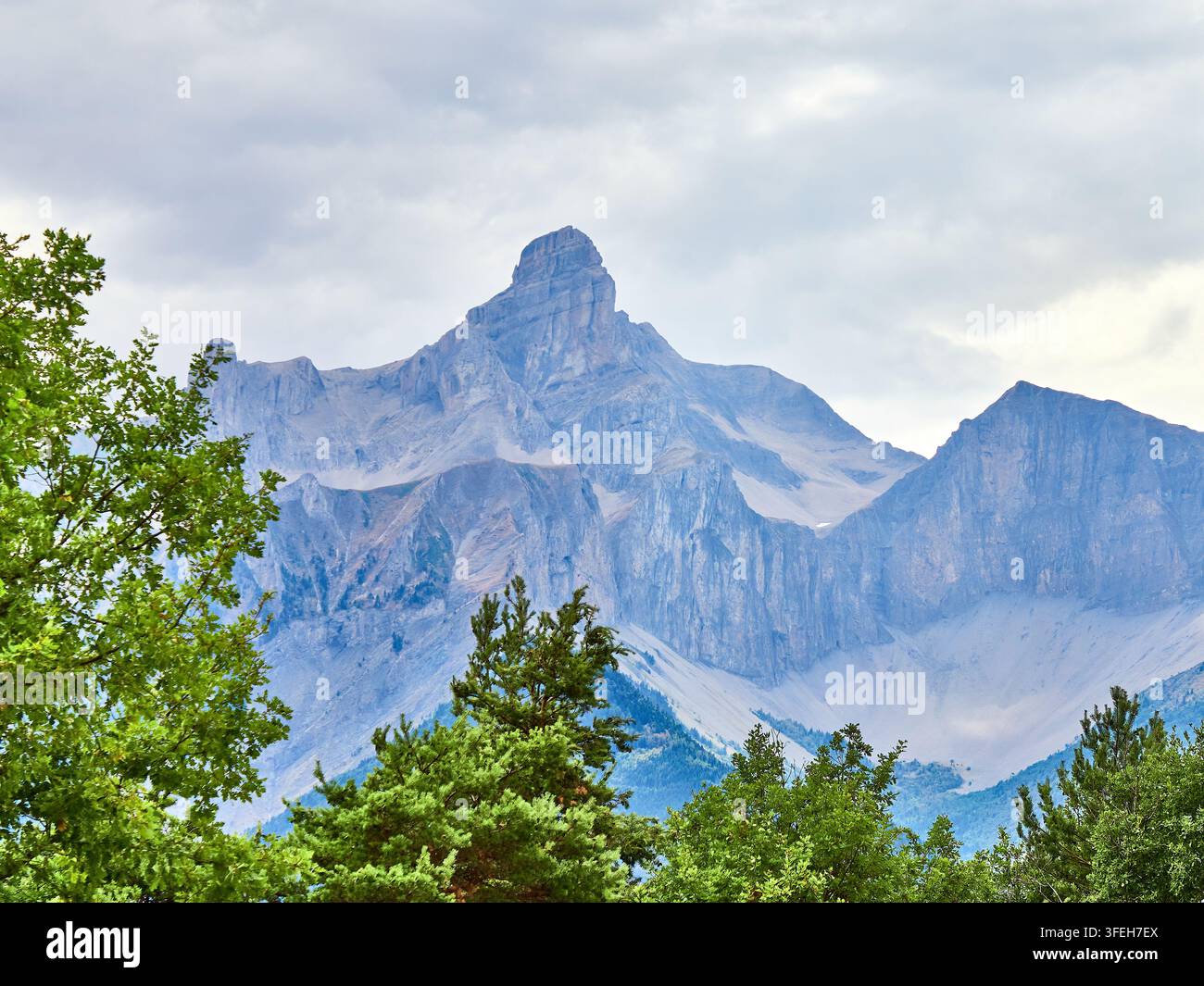 Picco drammatico delle Montagne Rocciose su un paesaggio alpino boscoso sotto un cielo nuvoloso Foto Stock