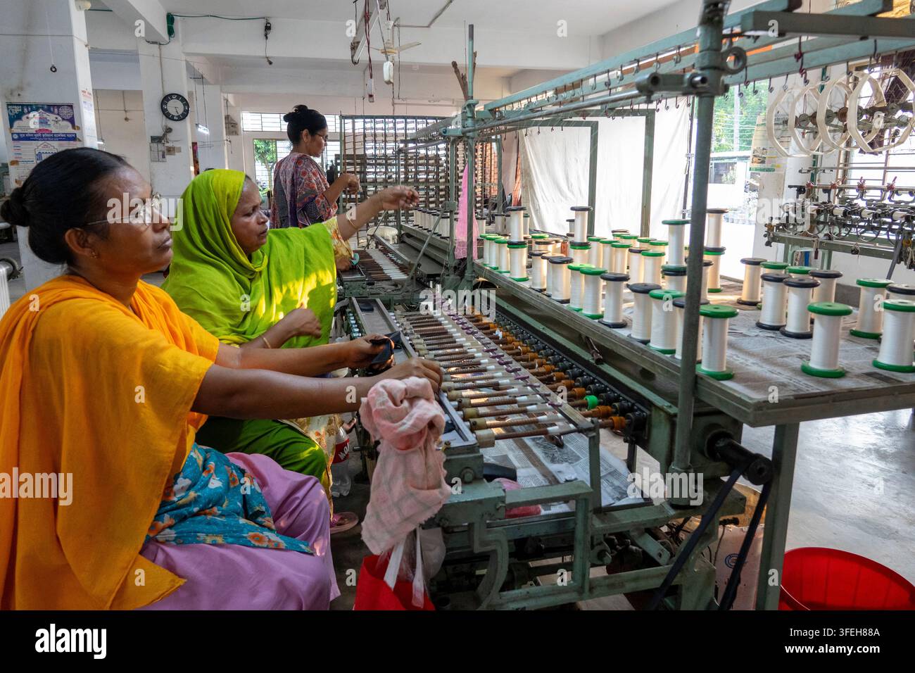 Donne che avvolgono filo di seta su bobine a una macchina tessile, Divisione di Dhaka, Dhaka, Bangladesh Foto Stock