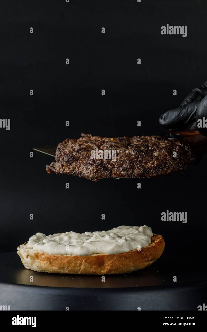 Lo chef posa una succosa polpetta di hamburger sul panino Foto Stock