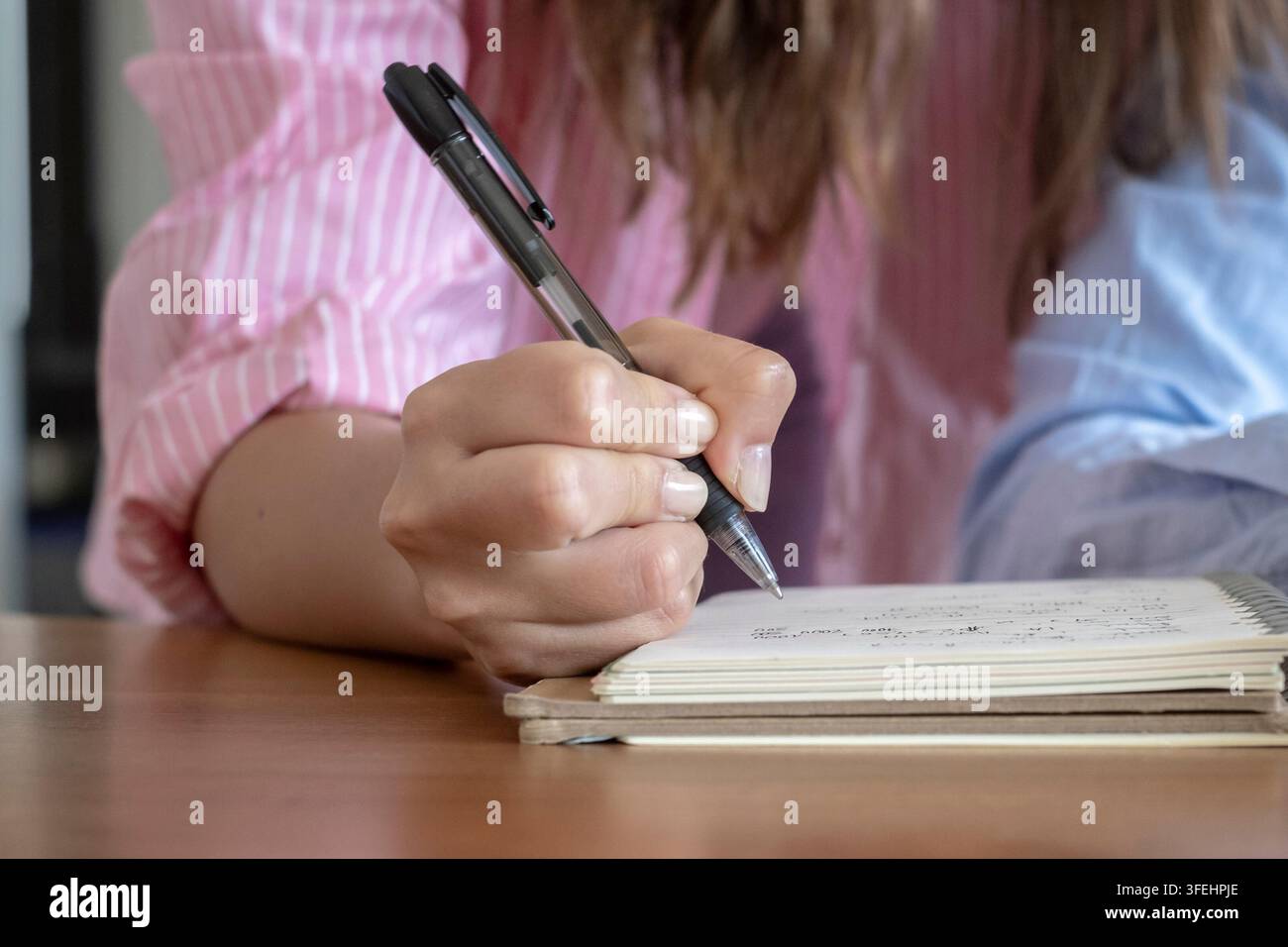 Prima di una mano che scrive appunti in un quaderno a spirale con una penna su una scrivania di legno, concetto di studio e pianificazione che mostra concentrazione, giornalismo, educazione Foto Stock