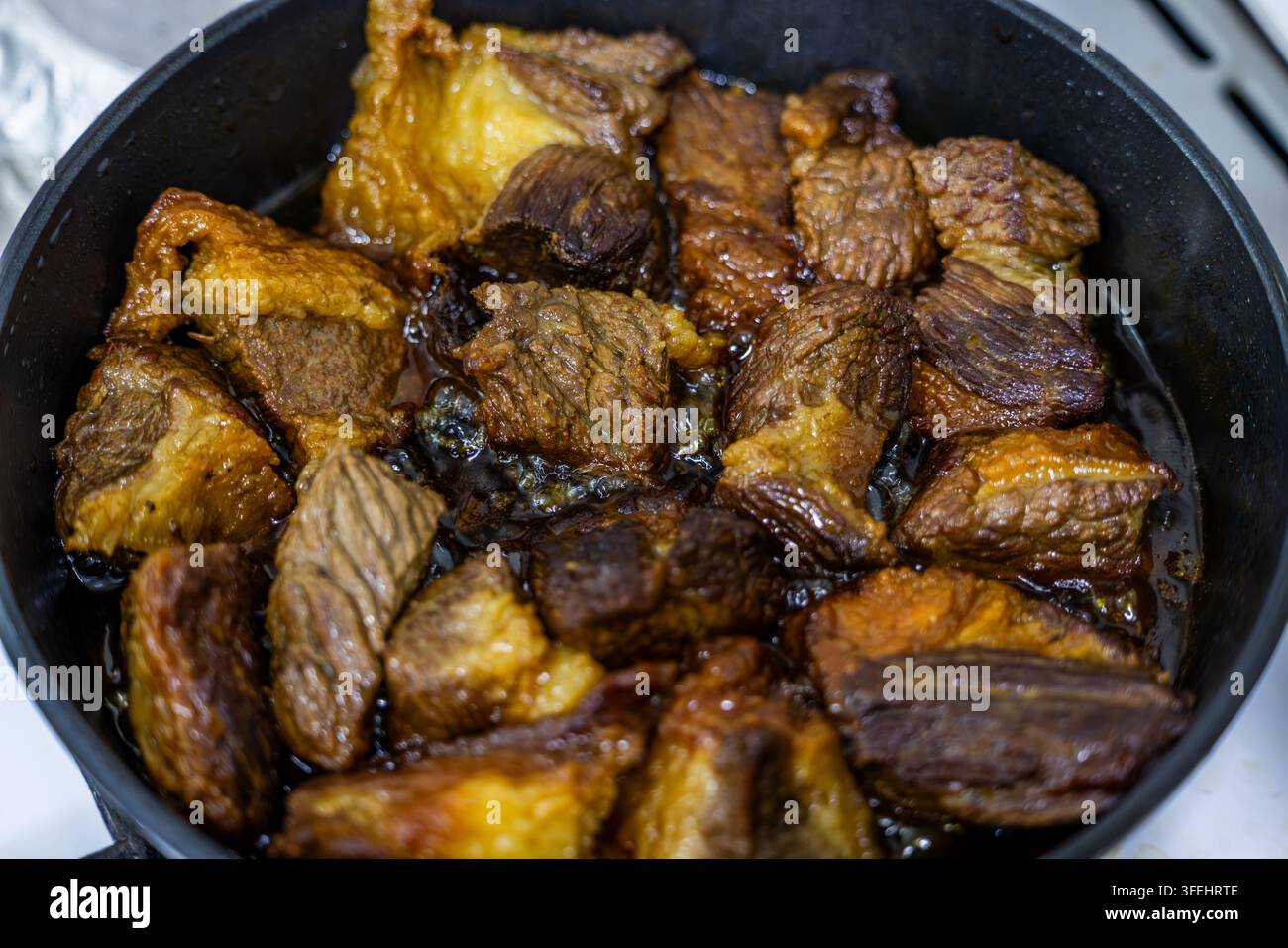 Primo piano dall'alto cattura pezzi di manzo succulenti che cuociono a fuoco lento in un liquido scuro. La texture ricca e il calore evocano un'esperienza culinaria sostanziosa. Foto Stock