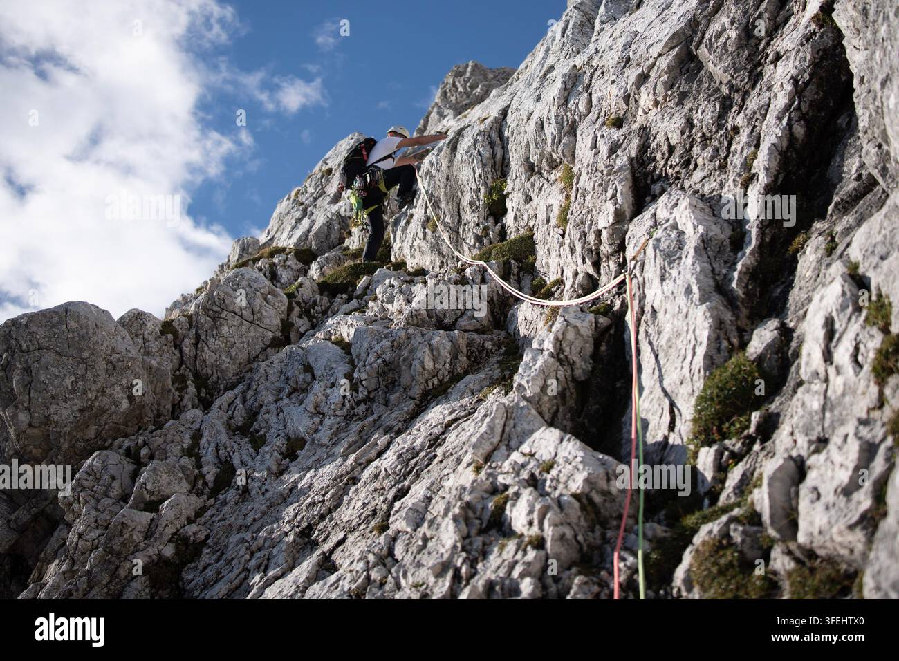 Arrampicatore che sale su una via multi-lunghezza su Alpspitze con doppie corde, indossa un'imbracatura e uno zaino su terreno calcareo ripido, arrampicata alpina Foto Stock