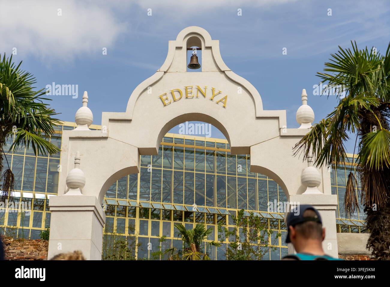 BRUGELETTE, BELGIO – 15 AGOSTO 2026: Arco ornamentale bianco con una campana e l'iscrizione Edenya davanti alla gigantesca serra Pairi Daiza Foto Stock