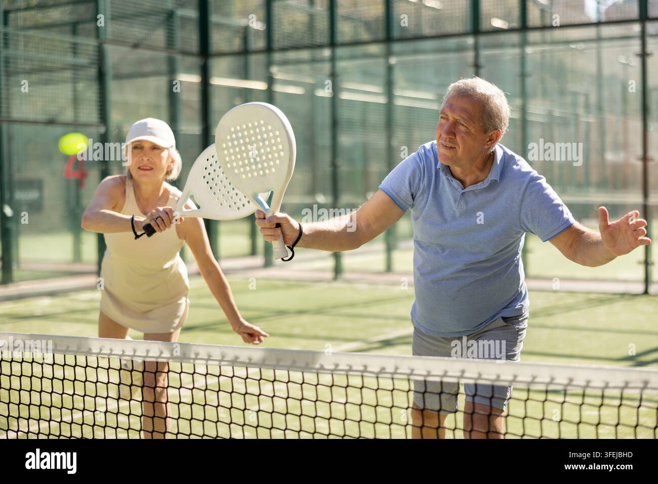 Uomo e donna anziani motivati che giocano a padel con il suo compagno di squadra in tribunale Foto Stock