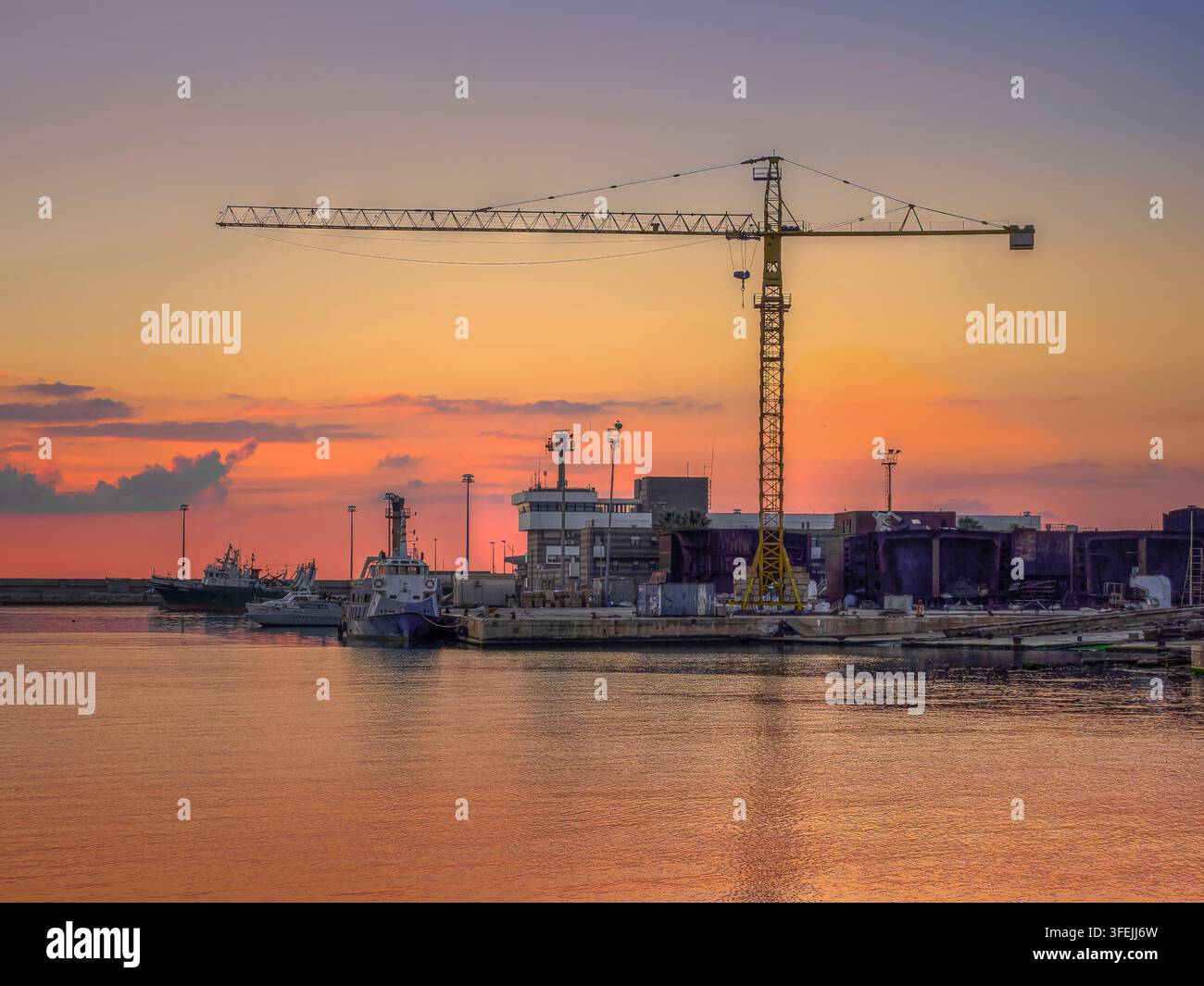 Scena portuale con una grande gru gialla che si affaccia sull'acqua al tramonto Foto Stock