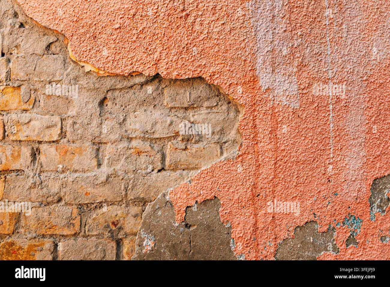 Intonaco rosa che si sfalda rivela il mattone esposto sottostante, creando una superficie ruvida e invecchiata per sfondi, progetti di design e ristrutturazione, rus urbano Foto Stock