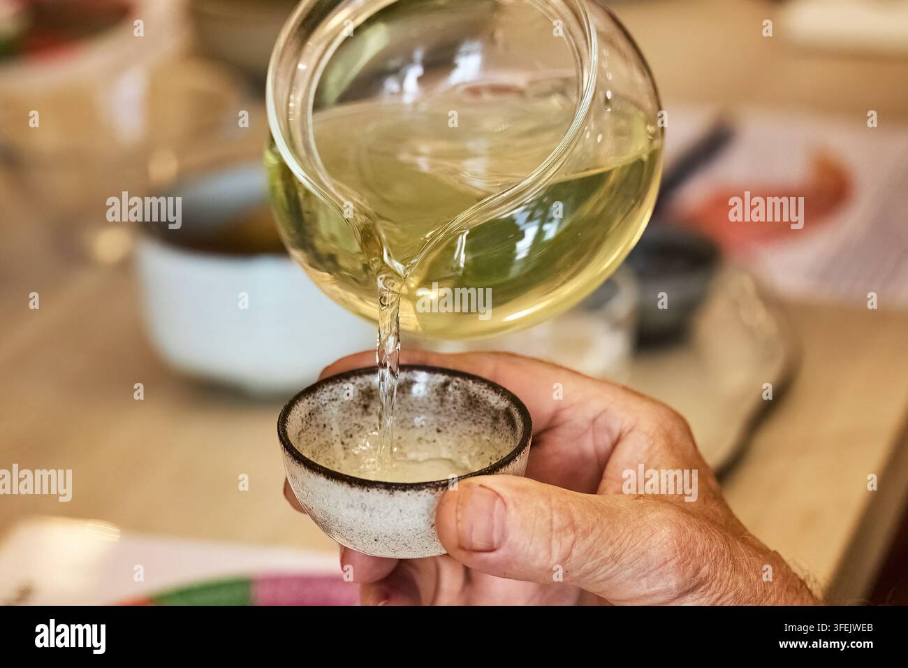 Mano che versa del tè verde da una teiera di vetro in una tazza Foto Stock
