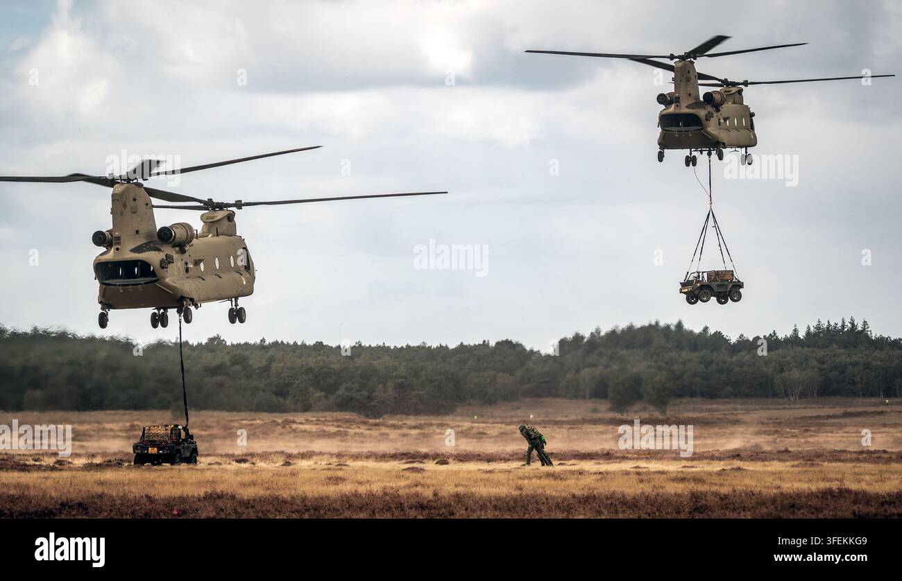 Veicoli fuoristrada militari trasportati con carico sospeso sotto gli elicotteri Boeing CH-47F Chinook durante un'operazione di sollevamento aereo militare. I Paesi Bassi Foto Stock