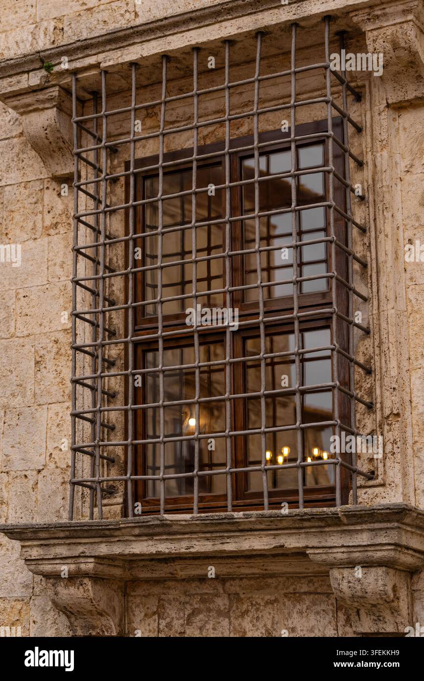 Finestra sbarrata su un edificio in pietra con luci calde che si riflettono attraverso il vetro Foto Stock