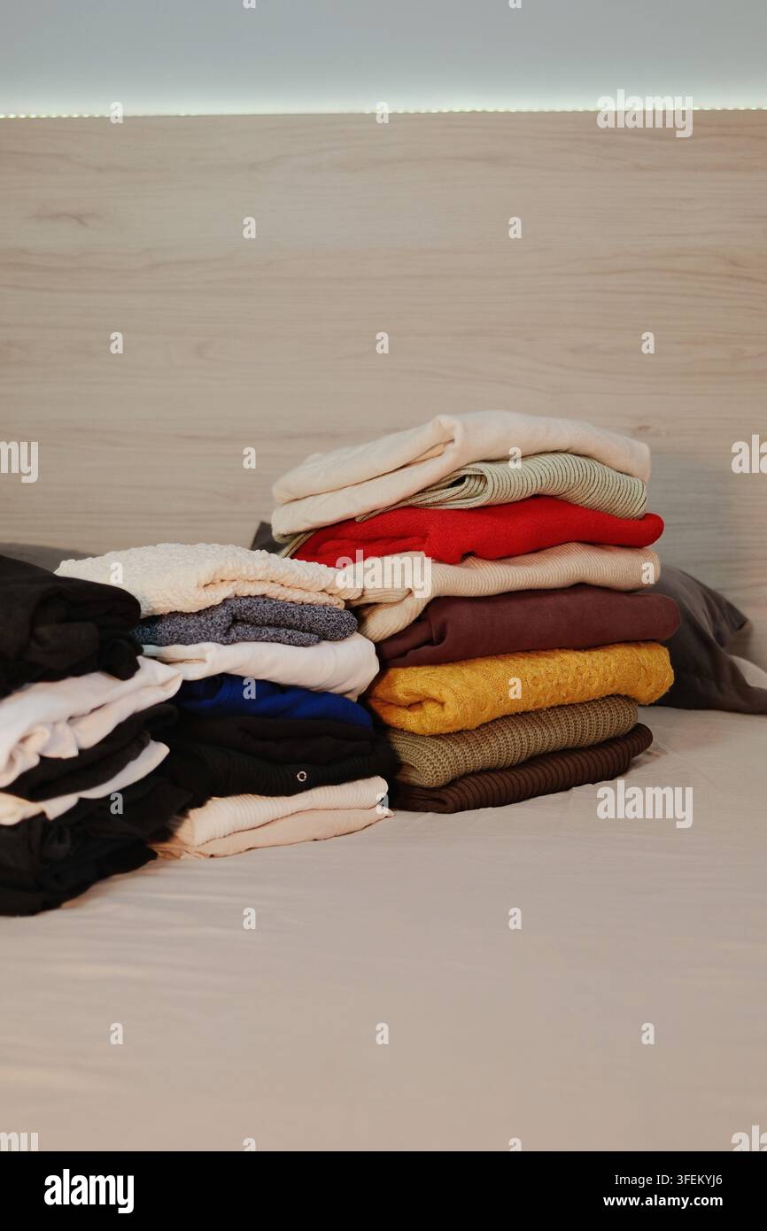 Composizione verticale di maglioni autunnali e invernali piegati disposti in piccoli mucchi su un letto, che mostra il sorting stagionale del guardaroba e l'organizzazione domestica. Foto Stock