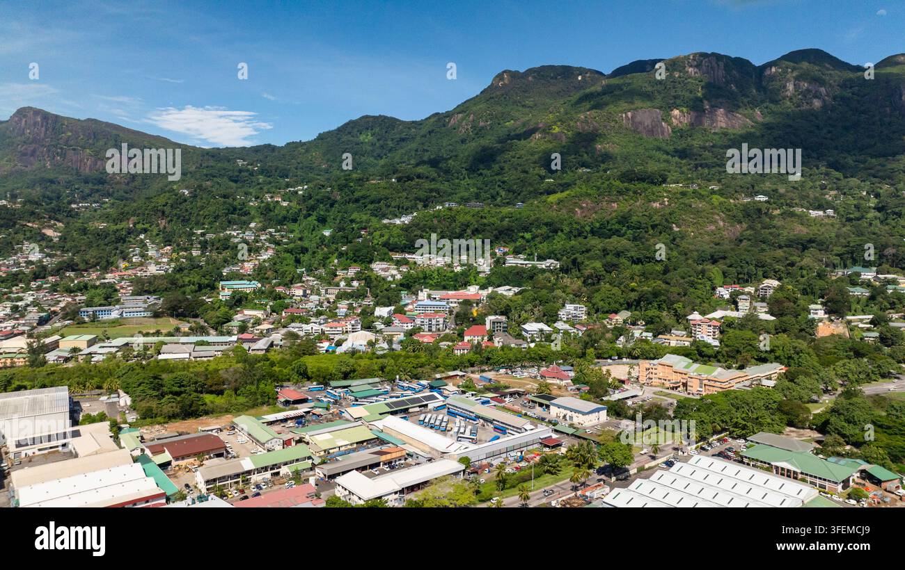 Area urbana con edifici residenziali e commerciali circondati da colline e montagne rigogliose di verde. Seychelles, Mahé. Victoria. Foto Stock