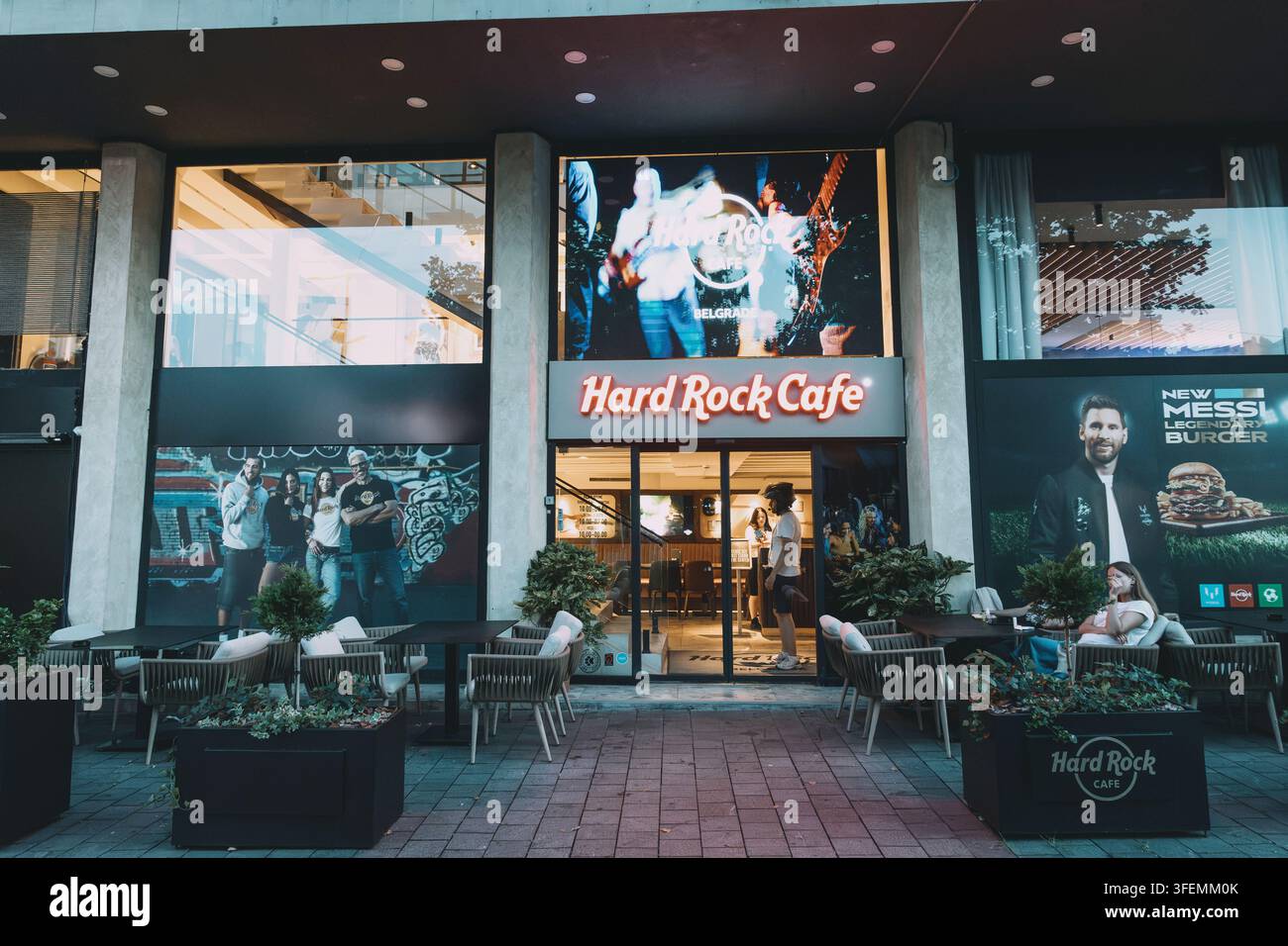 6 luglio 2026, Belgrado, Serbia: ingresso dell’Hard Rock Cafe con cartello luminoso, una video musicale in riproduzione e posti a sedere all’aperto su una strada cittadina Foto Stock