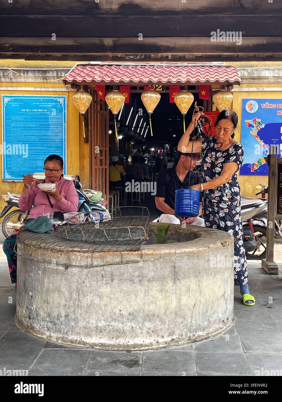 I residenti locali raccolgono acqua da un pozzo comunitario tradizionale situato davanti al mercato Cho Hoi An, Hoi An, Vietnam - 1 aprile 2026. Foto Stock