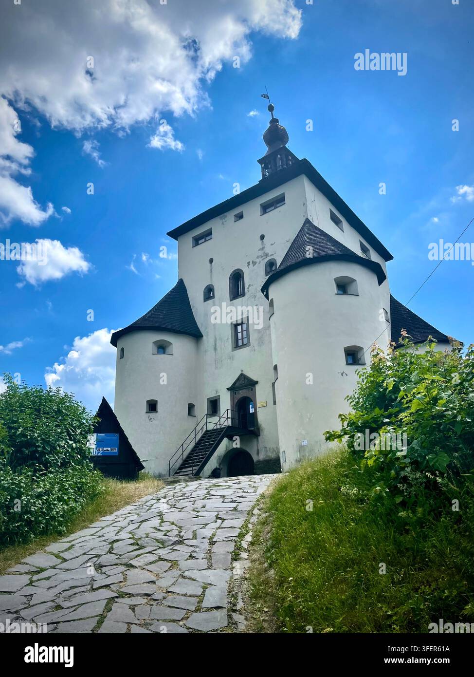 Foto verticale ad angolo basso del castello nuovo storico (Nový zámok) a Banská Štiavnica, Slovacchia, con bastioni bianchi e tetti di scandole scure - Immagine stock catturata con smartphone