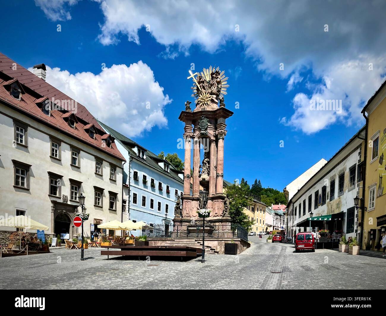 Foto verticale di Piazza Trinity a Banská Štiavnica, Slovacchia, che mostra la colonna barocca della Santa Trinità circondata da edifici storici - Immagine stock catturata con smartphone