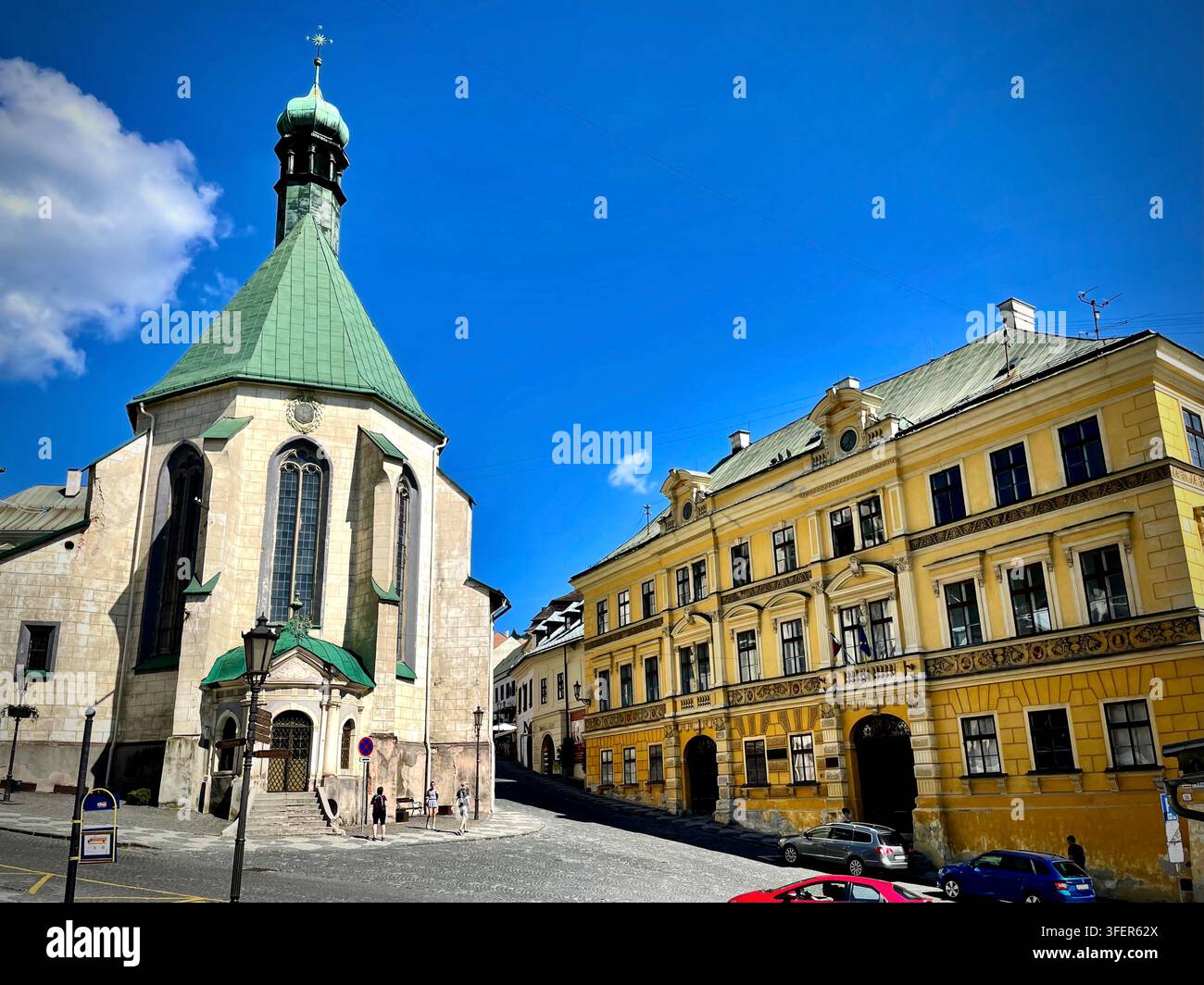 Foto verticale della storica Chiesa di Santa Elisabetta e degli edifici classicisti gialli circostanti a Banská Štiavnica, Slovacchia, con rame - Immagine stock catturata con smartphone