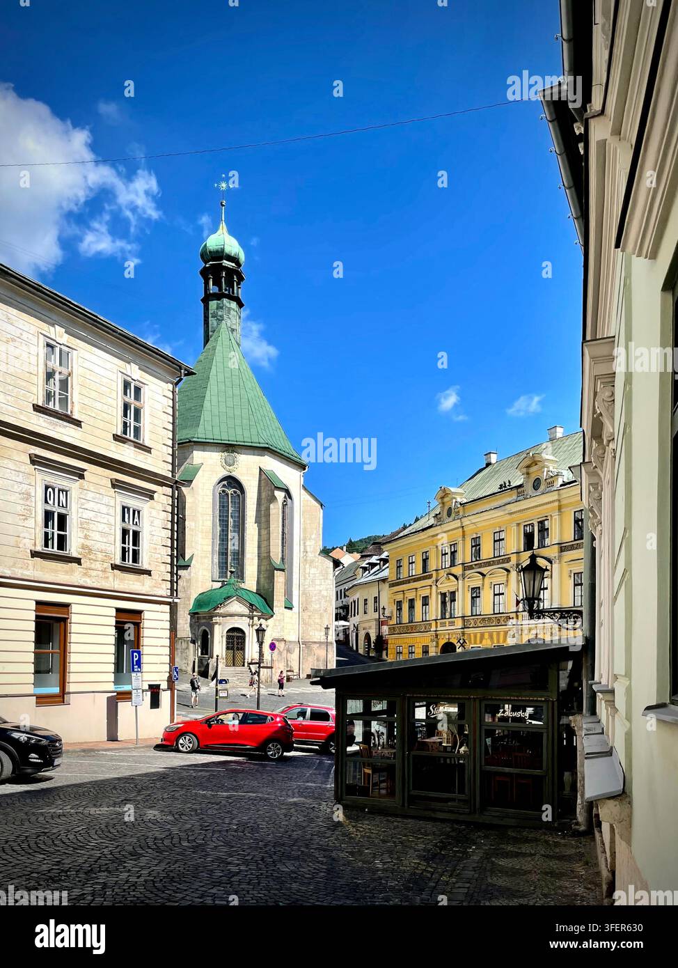 Foto verticale di Radničné námestie a Banská Štiavnica, Slovacchia, che mostra la chiesa gotica di Santa Elisabetta con il suo tetto di rame verde circostante - Immagine stock catturata con smartphone