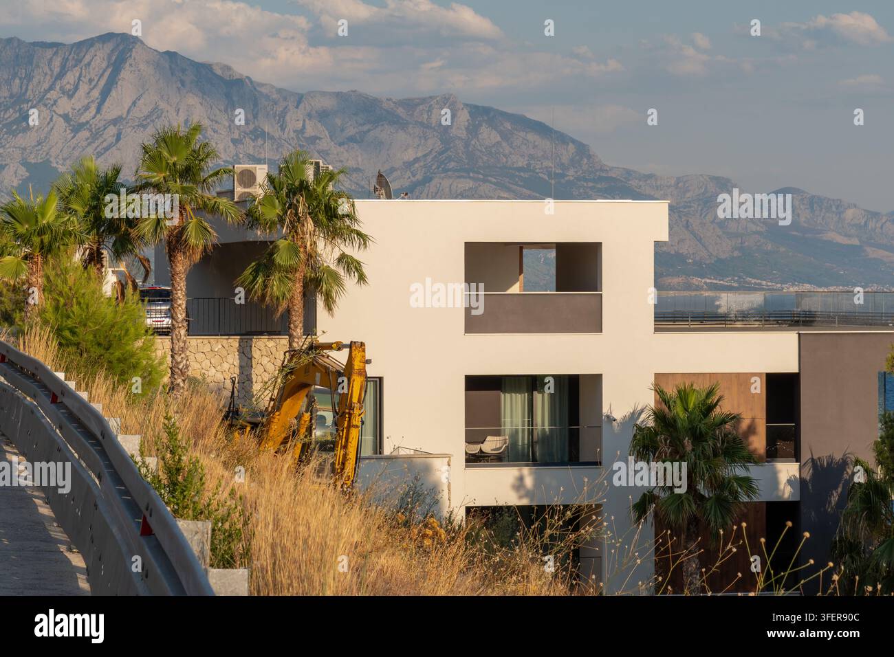 MIMICE, CROAZIA, 4 settembre 2026: Villa costiera moderna si erge tra le palme con le montagne che si stagliano sullo sfondo. Foto Stock