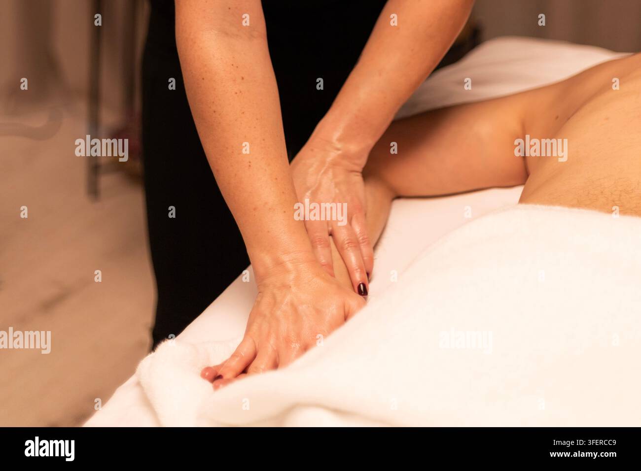 Prima vista di un massaggiatore che utilizza olio per massaggiare il piede di una persona su un lettino da massaggio coperto con un asciugamano bianco. Foto Stock