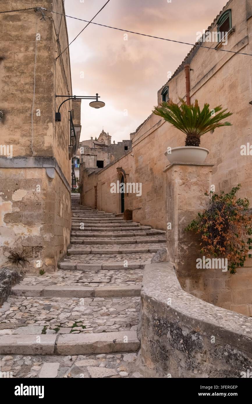Stretta strada acciottolata con scale in pietra al tramonto a Matera, Italia Foto Stock