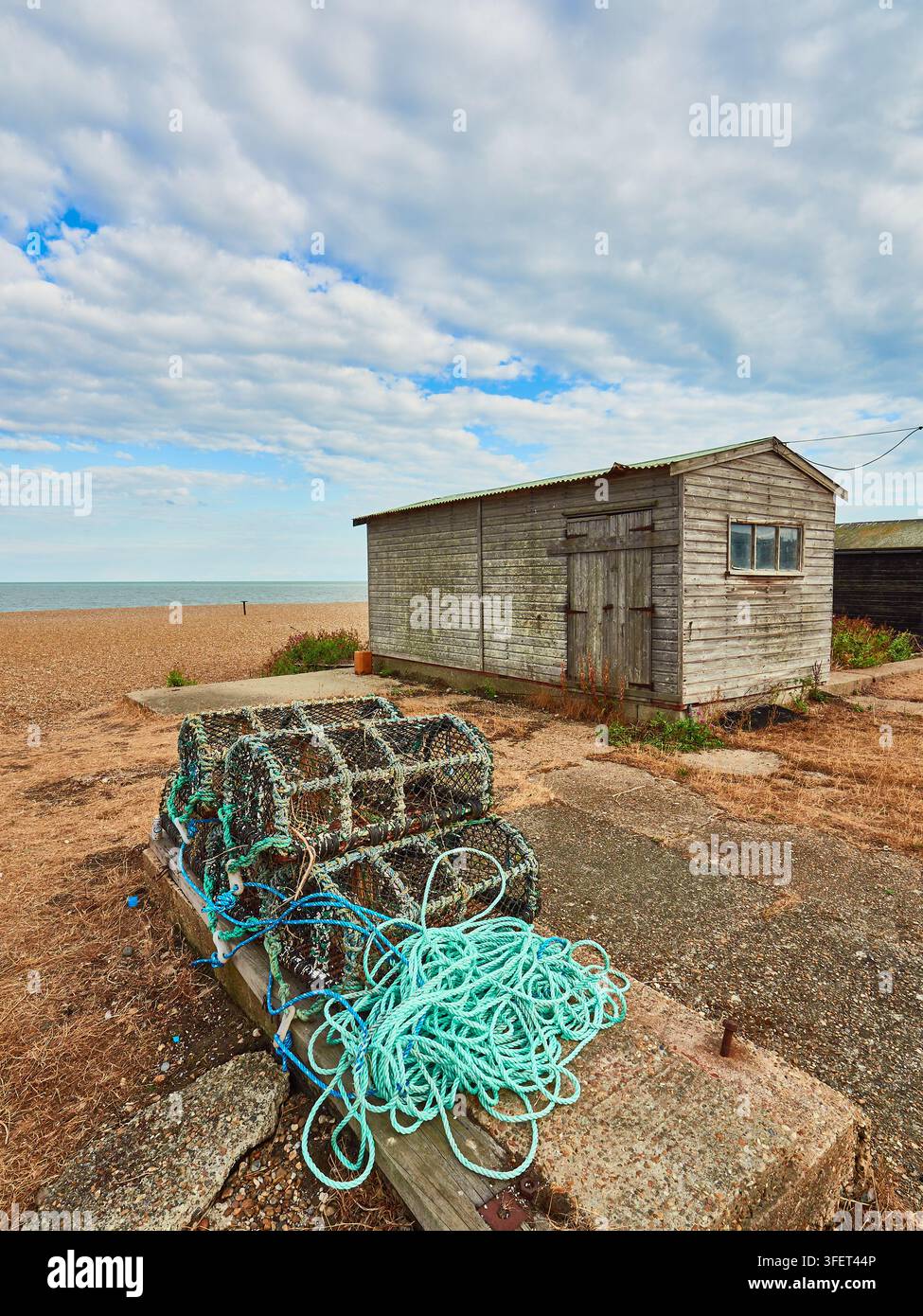 Capanni di pesca in legno e trappole per aragosta con corda brillante su una spiaggia di ciottoli sotto un cielo nuvoloso Foto Stock