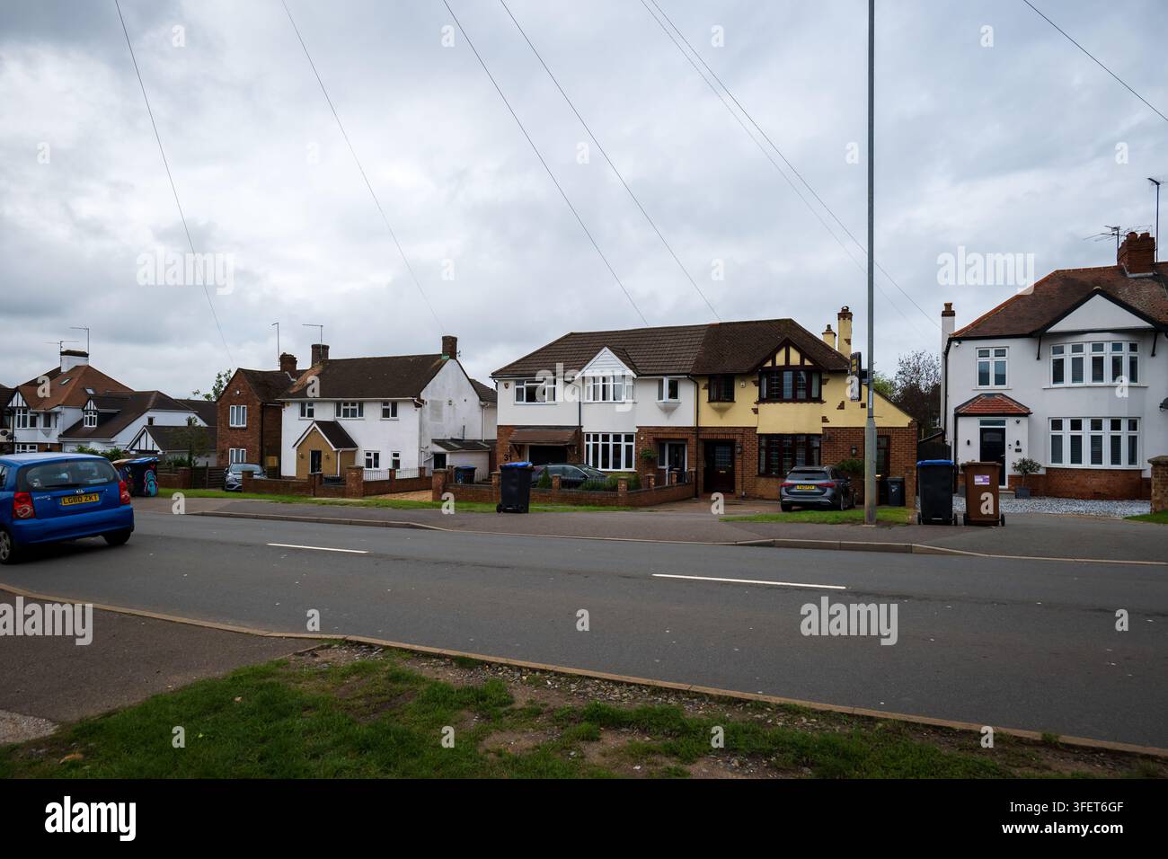 Via residenziale suburbana a Northampton, Regno Unito, che mostra case indipendenti e semi-indipendenti con vialetti, auto parcheggiate, giardini anteriori e bidoni con ruote Foto Stock