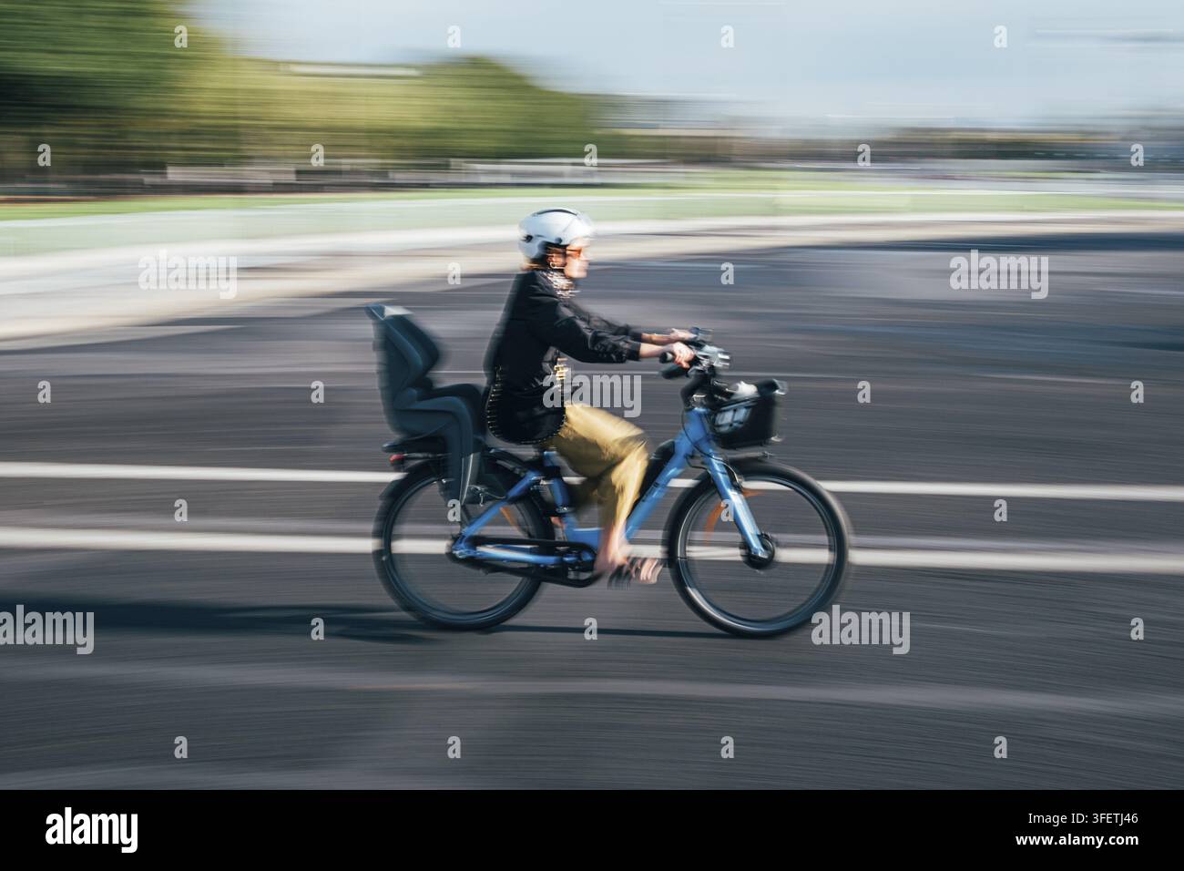 Ciclista femminile in sella a una e-bike blu su una strada, concentrandosi sulla dinamica del movimento grazie alla sfocatura del movimento sullo sfondo, Parigi, Île-de-France, Francia Foto Stock