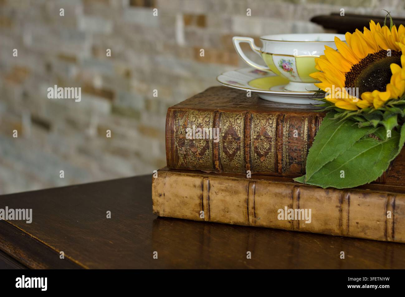 Tazza da tè vintage e piattino con un bouquet di girasoli disposti su libri rilegati in pelle antichi in un caldo interno tradizionale. Foto Stock