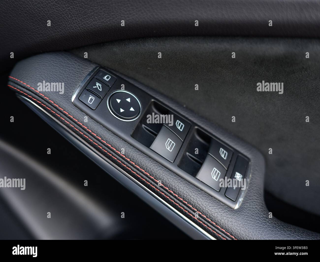 Primo piano di un pannello della portiera dell'auto. Pulsanti di controllo neri presentano funzioni di finestrino e specchietto. Puntini di cucitura marroni accentuano la superficie simile al cuoio. Veicolo scuro Foto Stock