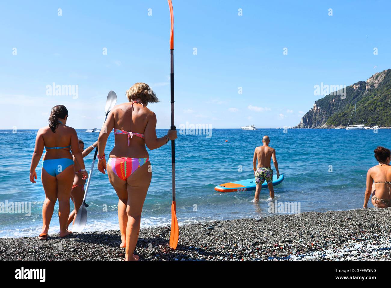 Riva Trigoso, ITALIA. 5 SETTEMBRE 2026. Persone attente alla salute con pagaie sulla spiaggia. Turisti attivi abbracciano le tendenze dello stile di vita fitness all'aperto Foto Stock