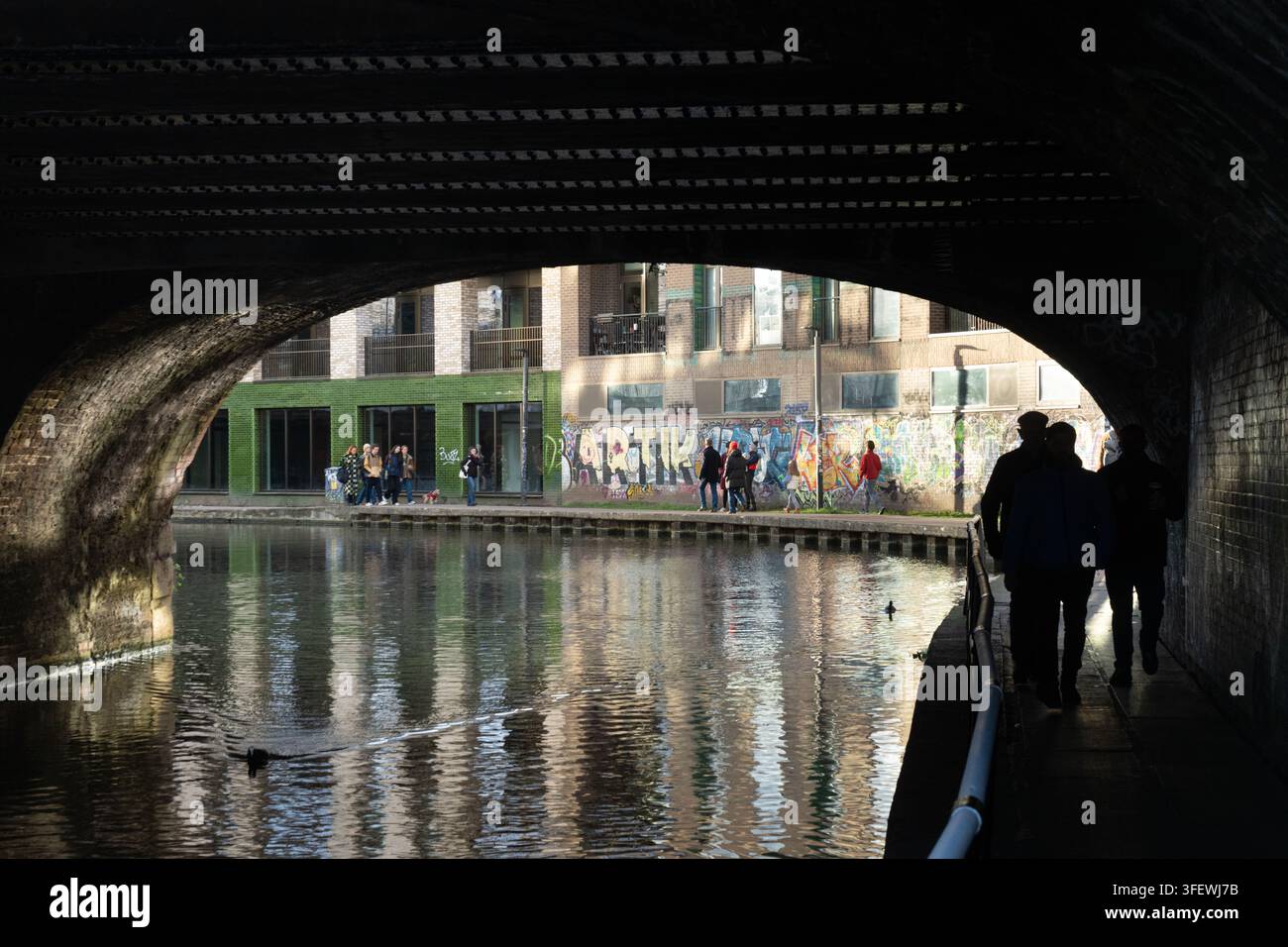 Le persone passeggiano lungo il sentiero del Regent's Canal a Londra, camminando sotto un ponte ferroviario per esercizio e svago. Foto Stock