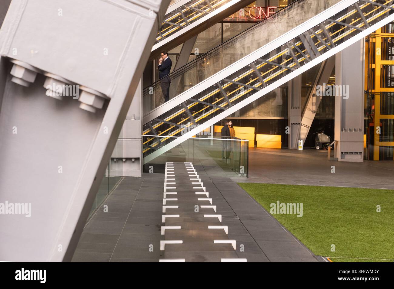 Un uomo d'affari sale una scala meccanica all'interno dell'iconico edificio high-tech di Lloyd a Londra, navigando nella famosa architettura interno-esterno. Foto Stock