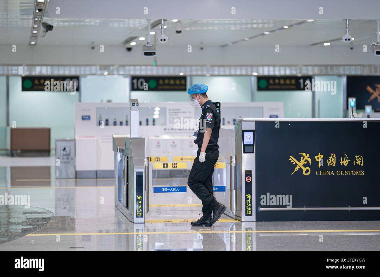 Un ufficiale doganale cinese in DPI si trova accanto ai cancelli di ispezione automatizzati all'aeroporto internazionale di Pechino Daxing durante la pandemia di COVID-19. Foto Stock
