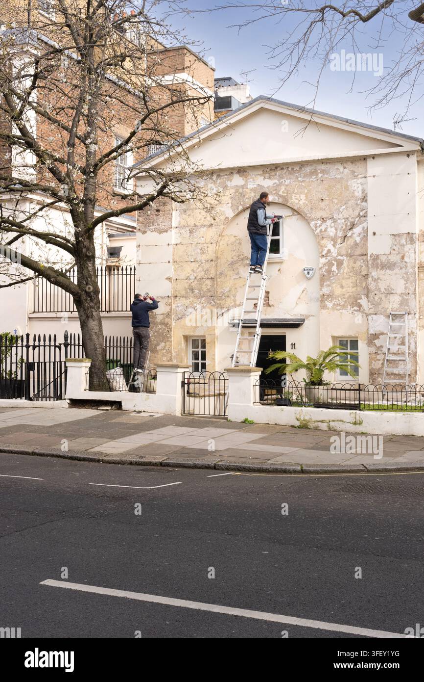 Due operai riparano la facciata danneggiata al 11 Eccleston Mews a Belgravia, Londra, restaurando l'esterno dell'edificio storico. Foto Stock