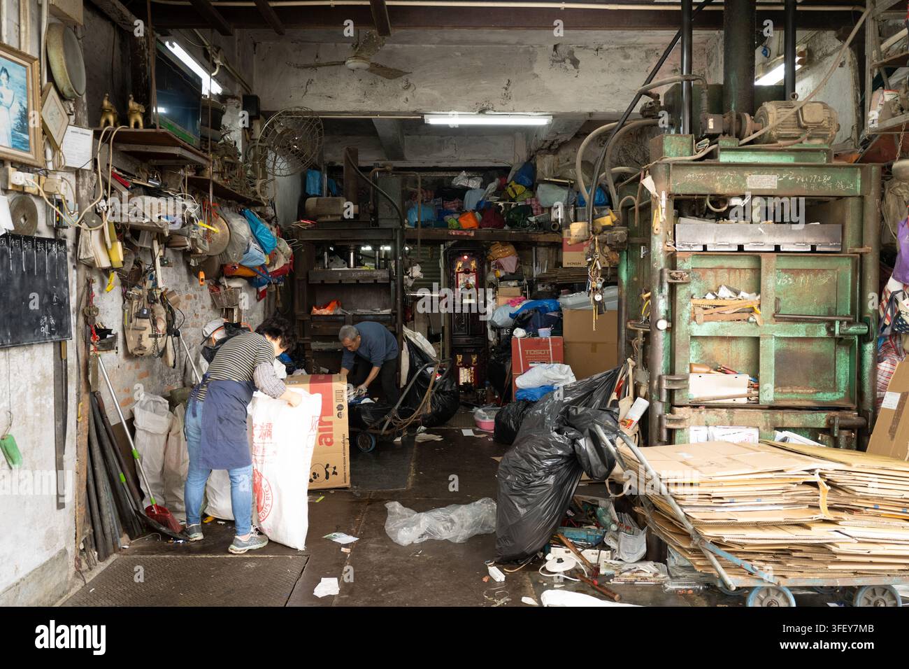 Due operai smistano e comprimono il cartone in un negozio di riciclaggio a Kennedy Town, Isola di Hong Kong, per elaborare i rifiuti locali. Foto Stock