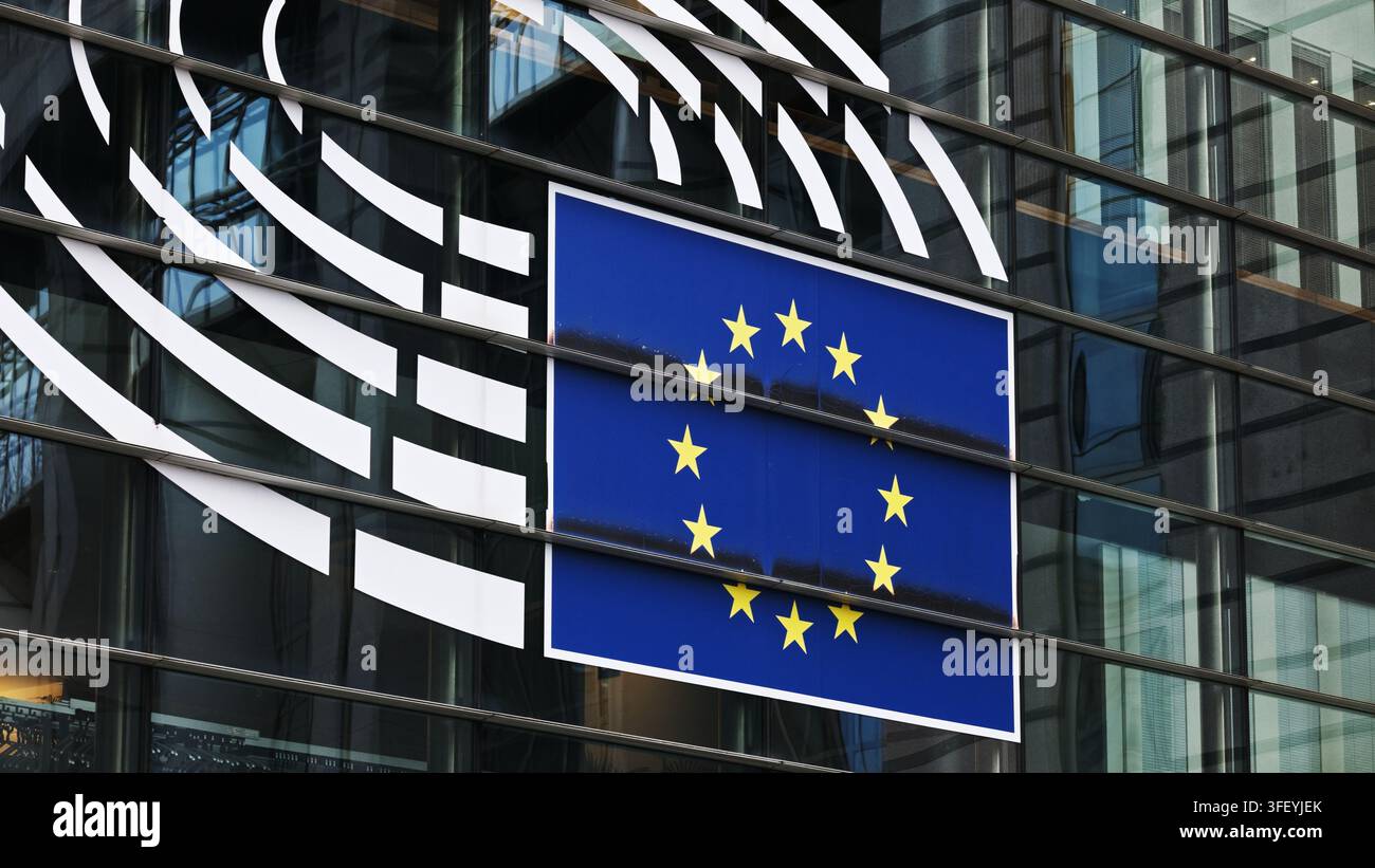 Bandiera blu con stelle gialle che decora una moderna facciata in vetro a Bruxelles durante le ore di luce Foto Stock