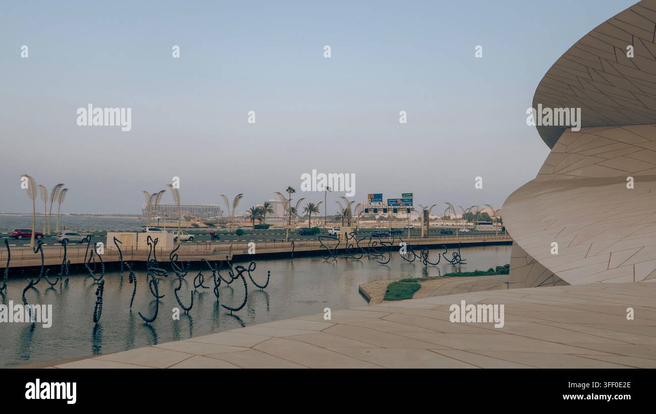 Scultura acquatica calligrafica nera moderna al Museo Nazionale del Qatar a Doha, con palme e lo skyline della città in lontananza. Foto Stock