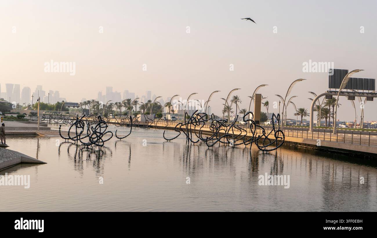 Scultura acquatica calligrafica nera moderna al Museo Nazionale del Qatar a Doha, con palme e lo skyline della città in lontananza. Foto Stock