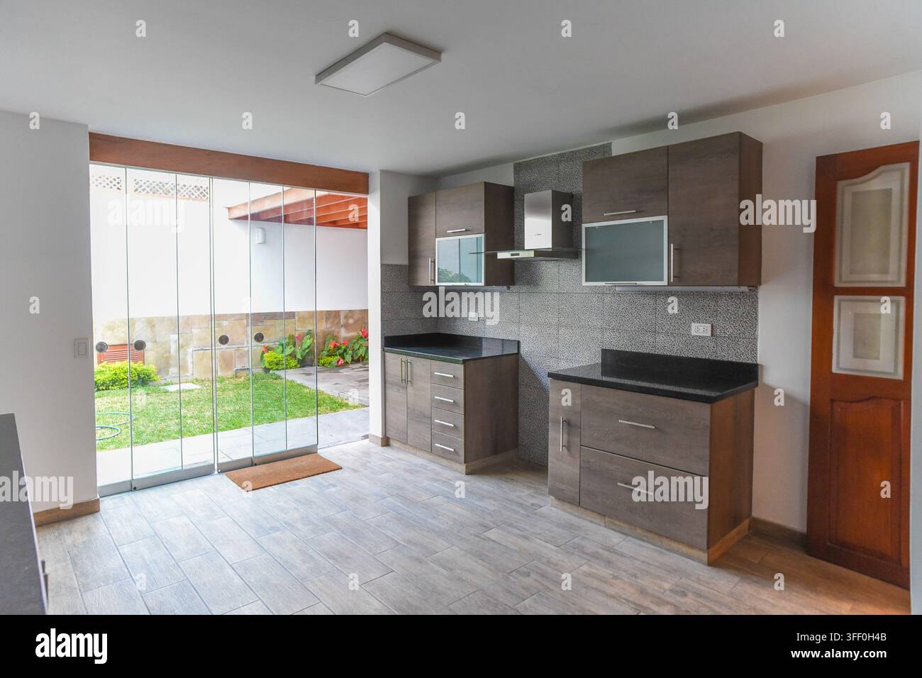 Cucina moderna con vista sul giardino: una cucina contemporanea con armadi eleganti e piani di lavoro in granito si apre su un giardino verde e vivace Foto Stock