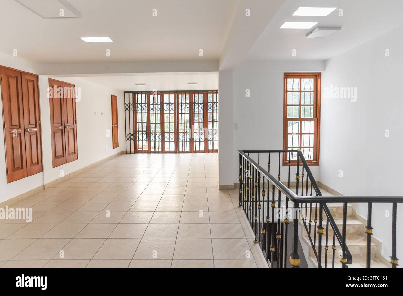 Corridoio vuoto con scale: Un corridoio luminoso e arioso con pavimenti piastrellati, porte di legno e una scala con ringhiera decorativa conduce Foto Stock