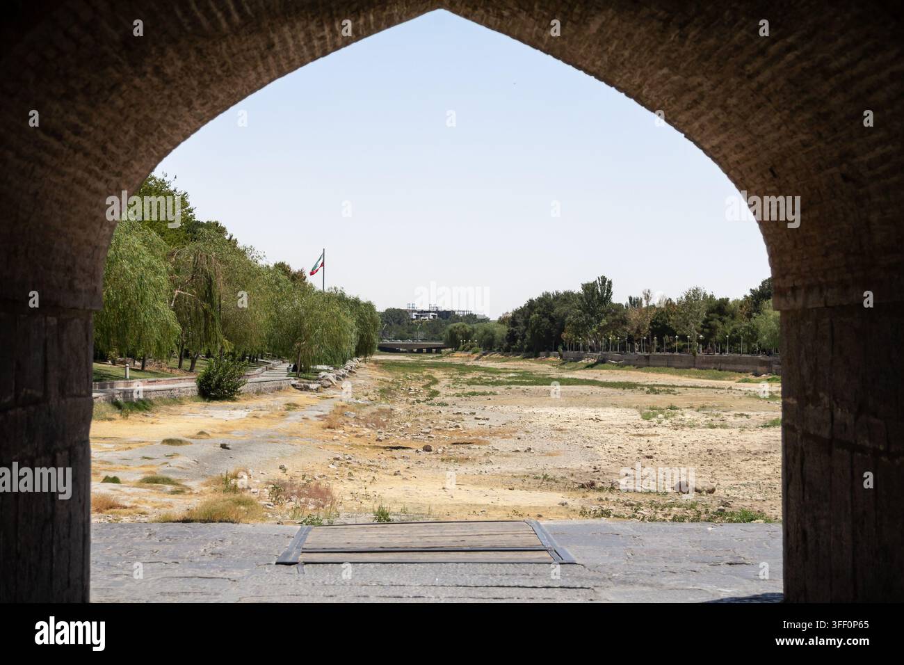 La bandiera iraniana sventola vicino al letto asciutto del fiume Zayandeh a Isfahan, Iran, dove la siccità e il caldo estremo estivo hanno lasciato il canale vuoto, illust Foto Stock