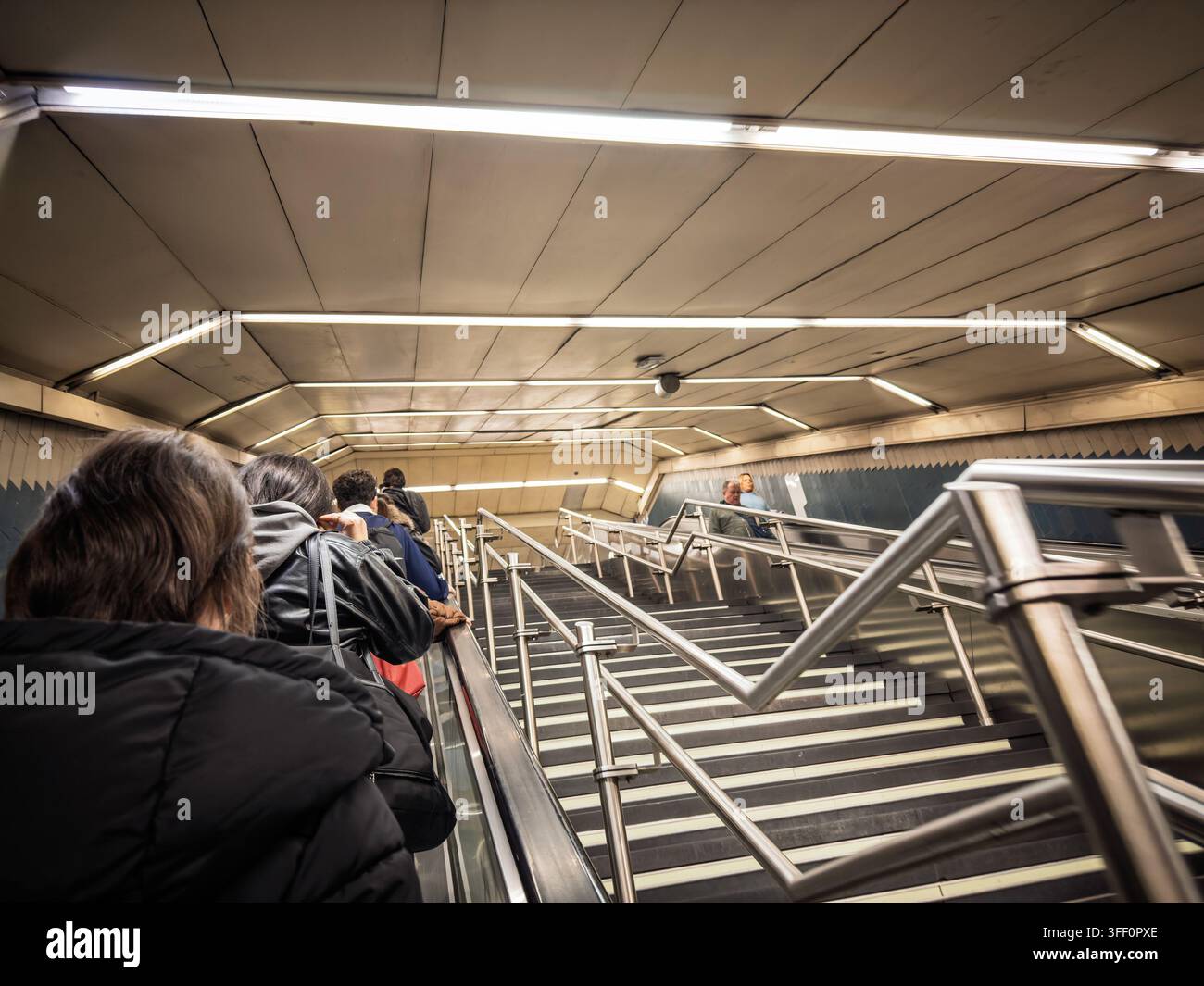 MADRID, SPAGNA - 24 FEBBRAIO 2026: Persone salgono su una scala mobile della metropolitana di Madrid, con corrimani metallici, illuminazione a striscia e il passaggio della stazione crea Foto Stock