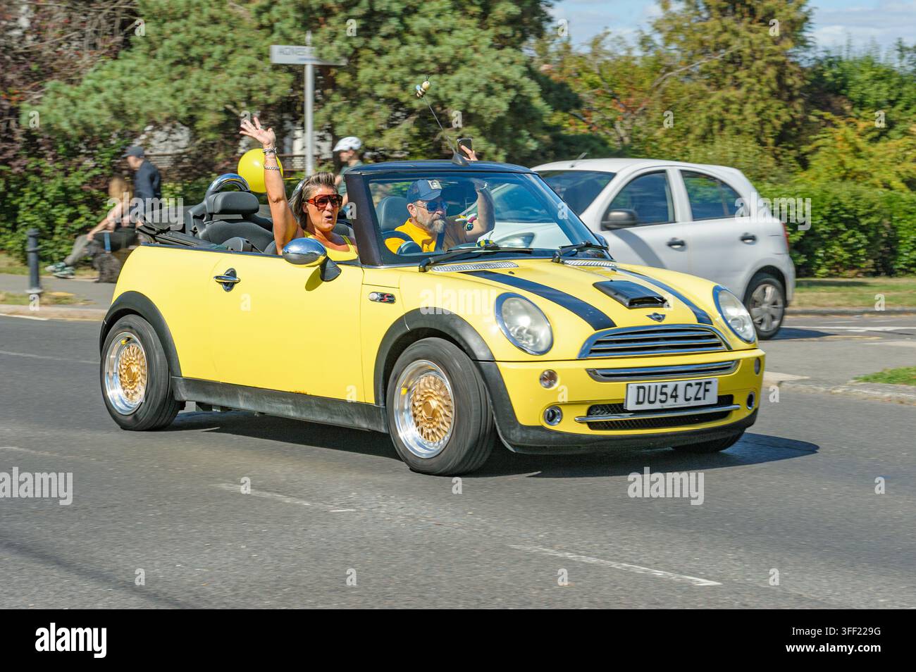 LEIGH-ON-SEA, UK – 5 SETTEMBRE 2026: Un passeggero saluta con entusiasmo da una Mini Cooper Convertible gialla durante la raccolta fondi "Go Gold" delle Gold Geese Foto Stock