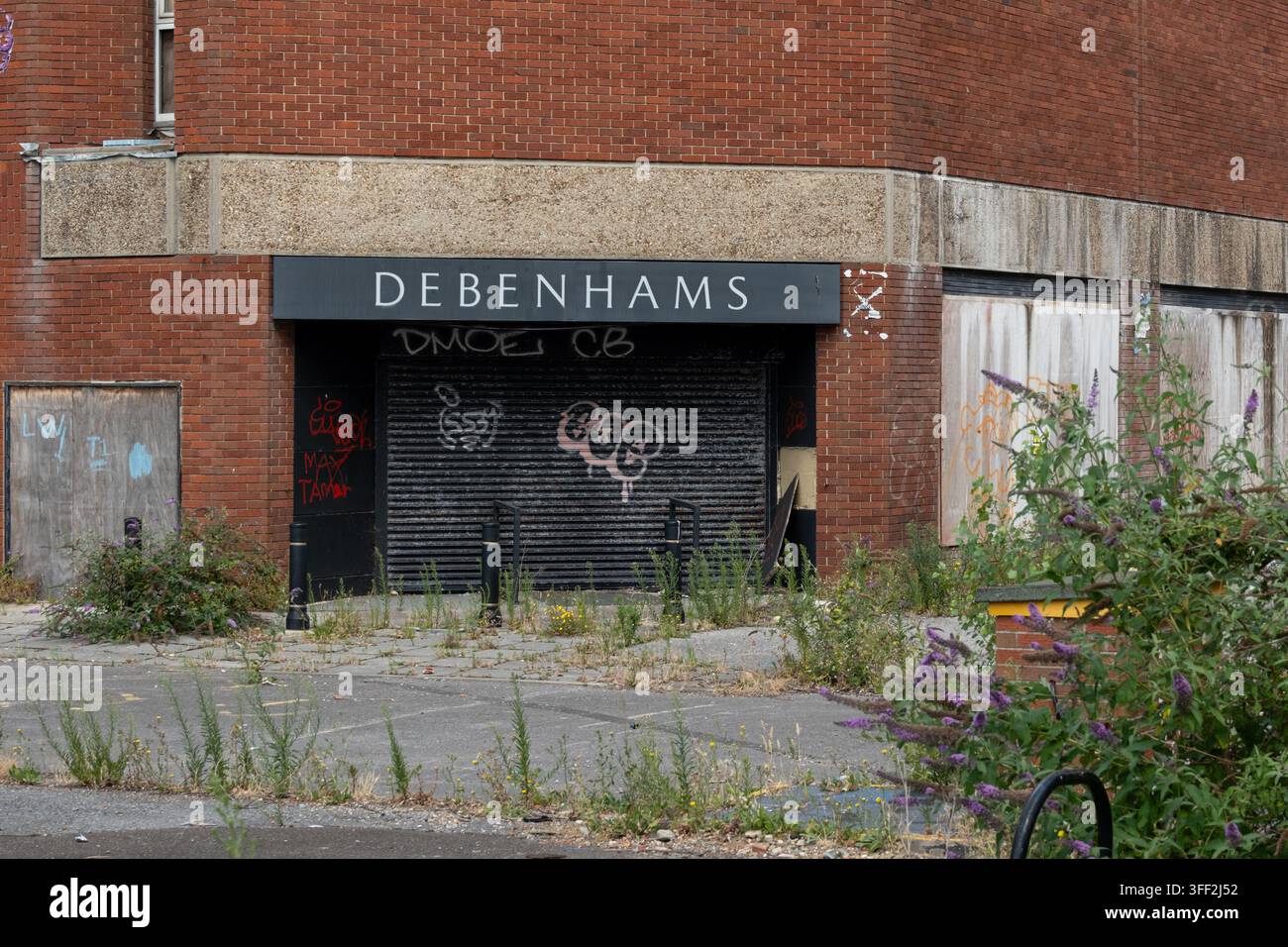 Ex ingresso posteriore di Debenhams a Portsmouth, serrande abbassate coperte di graffiti e parcheggio invaso dalla vegetazione. Foto Stock