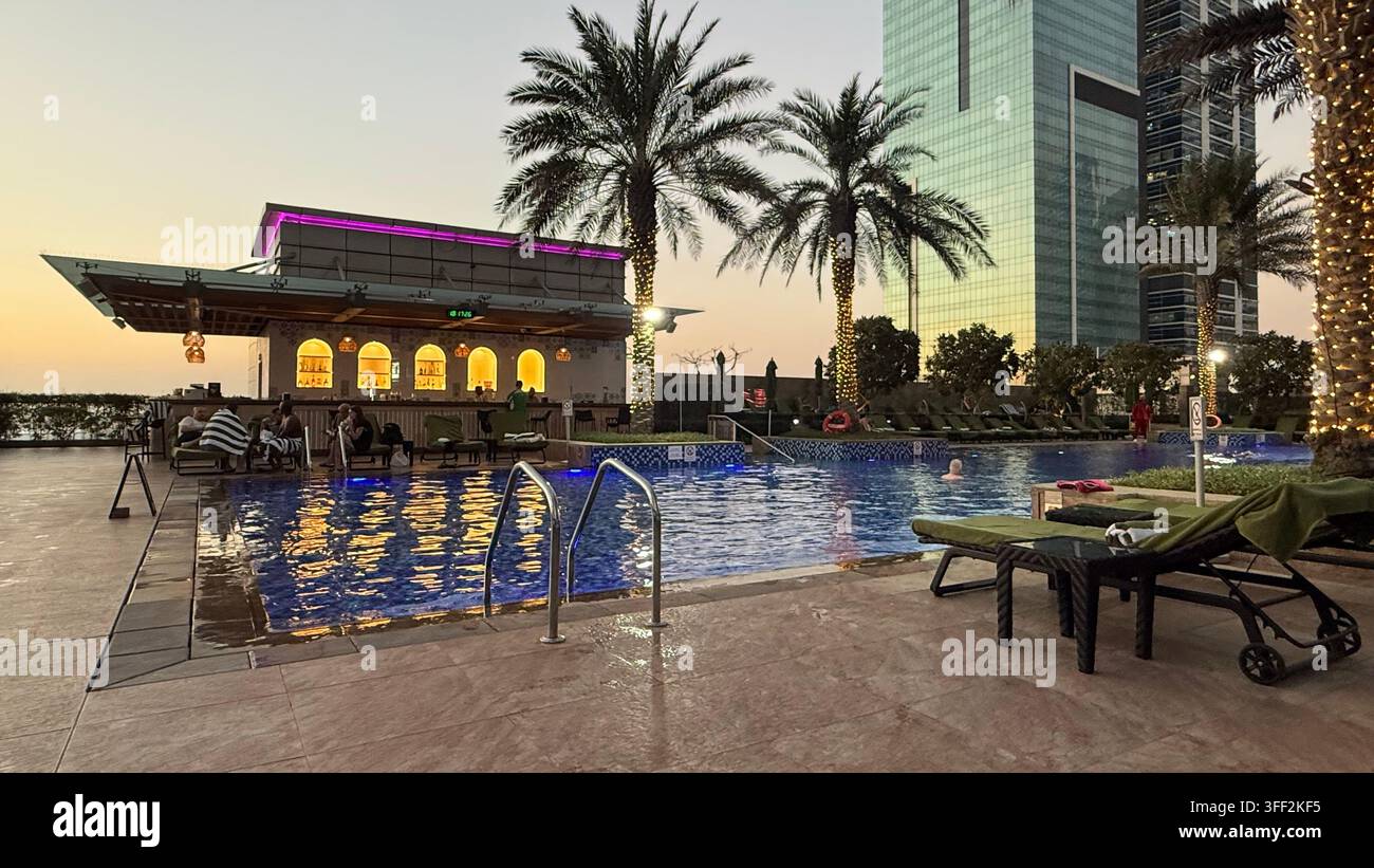 Ambientazione del primo pomeriggio sopra il bar della piscina e il ponte della piscina all'aperto illuminato al JW Marriott Marquis Hotel Dubai sulla Sheikh Zayed Road nel bus - Immagine stock catturata con smartphone