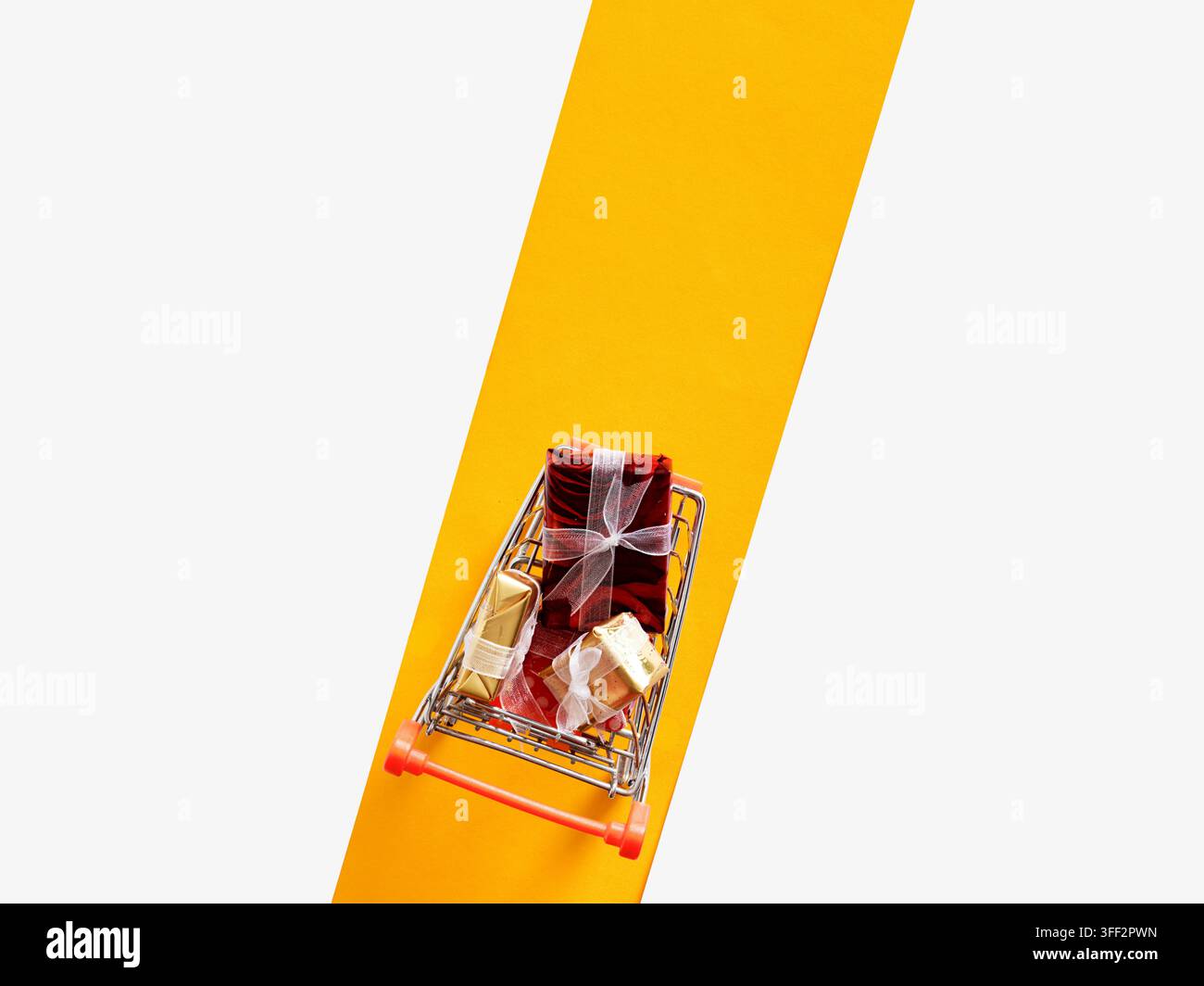 Carrello della spesa in miniatura con regali incartati, concetto di acquisto e consumismo Foto Stock