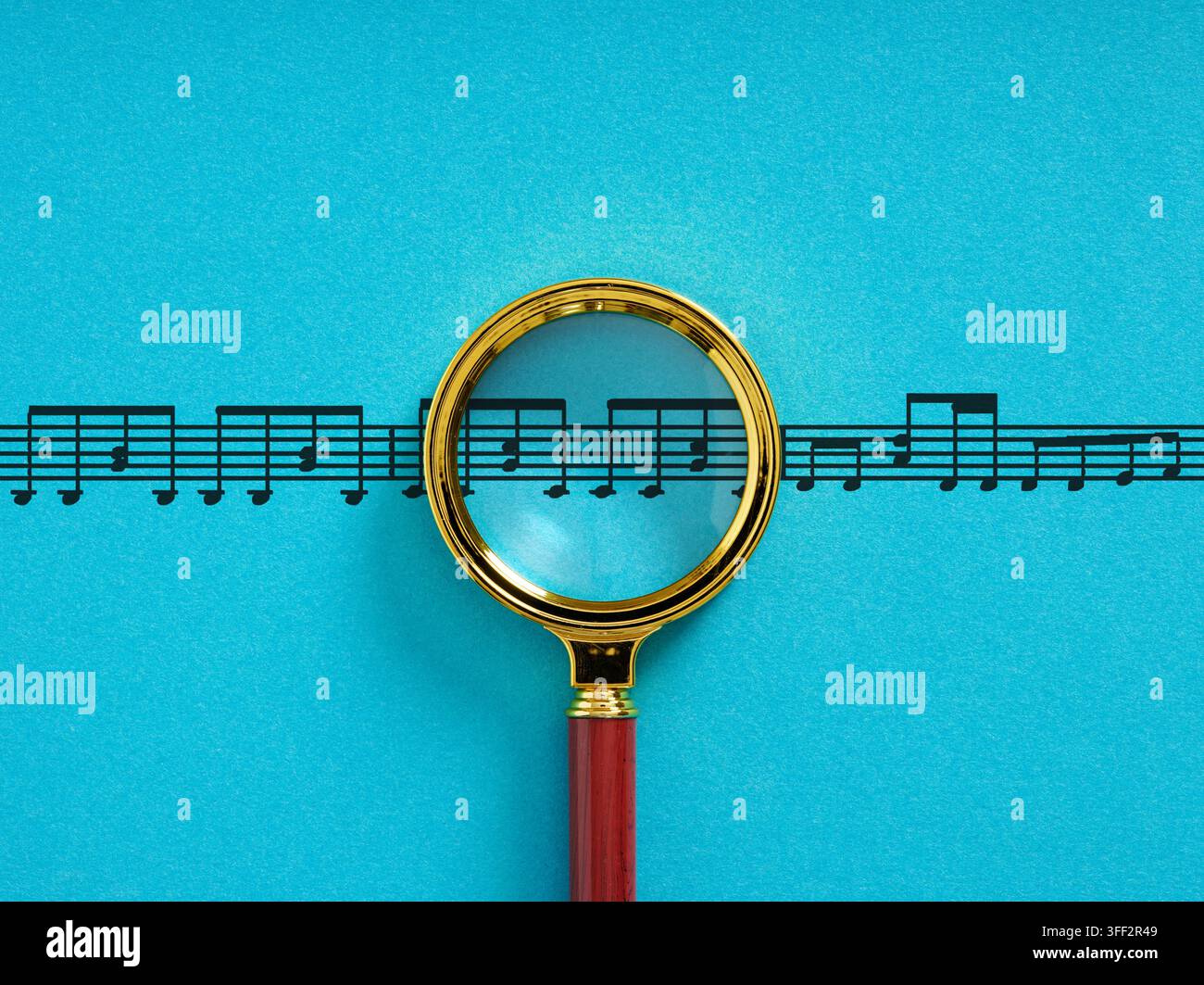 Lente d'ingrandimento che esamina una partitura con note e composizione su sfondo blu Foto Stock